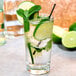 A glass of water with limes and mint with a black straw.