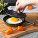 A hand holds a Lodge mini cast iron skillet with a lid over an egg.