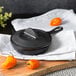 A Lodge mini cast iron skillet with a lid on a wooden cutting board with orange peppers.