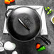 A black Lodge cast iron grill pan with eggs, peppers, and other ingredients.