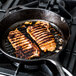 Two pork chops cooking in a Lodge cast iron grill pan.