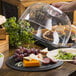 A person using a Tablecraft Faux Slate Melamine Tray to cover a plate of food with a glass dome.