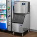 A Manitowoc water cooled ice machine next to a vending machine.