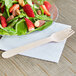 A wooden fork next to a plate of salad with strawberries and nuts.