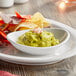 A white Acopa porcelain bowl of guacamole with chips on a table.