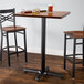 A Lancaster Table & Seating black cast iron bar height table base with two chairs and glasses on a wooden table.