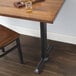 A wooden table with a Lancaster Table & Seating black cast iron end column table base with self-leveling feet and a glass of alcohol on it.