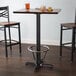 A Lancaster Table & Seating black cast iron bar height table base with a metal foot ring and self-leveling feet.