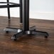 A Lancaster Table & Seating black metal bar height table base with self-leveling feet.