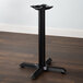 A Lancaster Table & Seating black cast iron table base with a black pole on a wood floor.