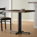 A black Lancaster Table & Seating cast iron table base with a wooden top and two chairs.