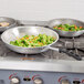 A Vollrath Wear-Ever fry pan with vegetables in it on a stove.