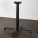 A Lancaster Table & Seating black cast iron table base on a wood floor.