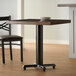 A Lancaster Table & Seating black cast iron table base with a wooden table top and two chairs with a plate on top.