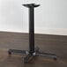 A Lancaster Table & Seating black cast iron table base with a pedestal column on a wood floor.