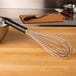 A Matfer Bourgeat stainless steel piano whisk in a bowl on a wood surface.