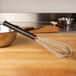 A Matfer Bourgeat stainless steel whisk with an Exoglass handle on a wooden surface.