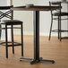 A black Lancaster Table & Seating bar height table base with self-leveling feet on a table with two stools.