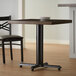 A black Lancaster Table & Seating cast iron table base with FLAT Tech levelers under a wooden table in a restaurant.