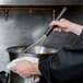 A chef using a Matfer Bourgeat stainless steel whisk to stir a pot.
