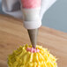 A person using an Ateco oval tip in a pastry bag to frost a cupcake.
