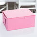 A close-up of a 6 1/2" x 4" x 2 3/4" pink bakery box with a lid on a white surface.