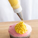 A cupcake with yellow icing piped using an Ateco curved petal piping tip.