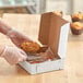 A person in gloves putting a croissant in a white bakery box.