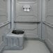 A wheelchair accessible grey PolyJohn portable restroom with a black seat.