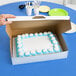 A hand cutting a frosted cake in a white bakery box.