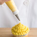 A person using an Ateco leaf frosting tip and pastry bag to pipe yellow frosting on a cupcake.