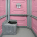 A PolyJohn pink and grey wheelchair accessible portable restroom with a black toilet seat.