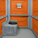 A PolyJohn orange wheelchair accessible portable restroom with a black toilet seat.
