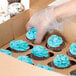 A hand putting blue frosting on cupcakes in a Baker's Mark kraft window cupcake box with a 12 slot insert.