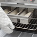 A person using an oven mitt to remove trays of Chicago Metallic bread loaves from an oven.