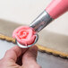 A person using an Ateco rose piping tip to pipe pink frosting on a cake.