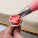 A person using an Ateco rose piping tip with pink frosting to decorate a cake.