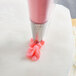 A person using an Ateco drop flower piping tip with a pink frosting bag to pipe pink flowers on a white cake.