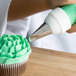 A person using an Ateco left-handed curved petal piping tip to decorate a cupcake with green frosting.