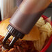A close up of a Vollrath Traex Color-Mate squeeze bottle with brown cap pouring sauce over pulled pork.