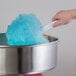 A white cotton candy cone being used to hold blue cotton candy above a metal cotton candy machine.