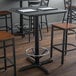 A black Lancaster Table & Seating bar height table base with a foot ring on a table in a restaurant.