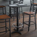 A Lancaster Table & Seating black cast iron bar height table base with a foot ring under a table with chairs.