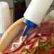A hand using a Vollrath Color-Mate squeeze bottle with a blue cap to put sauce on a sandwich.