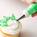 A hand using an Ateco leaf piping tip to decorate a cupcake with green icing.