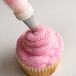A person using an Ateco French Star piping tip to frost a cupcake with pink frosting.