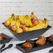 A G.E.T. Enterprises Bugambilia black resin-coated aluminum bowl holding fruit and muffins on a table in a hotel buffet.