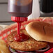 A hamburger bun with a squeeze bottle of ketchup on the table.