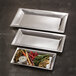 Three American Metalcraft rectangular hammered stainless steel trays with vegetables and dip on a counter.
