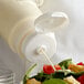 A salad being poured from a Vollrath Traex wide mouth squeeze bottle cap converter onto a salad.